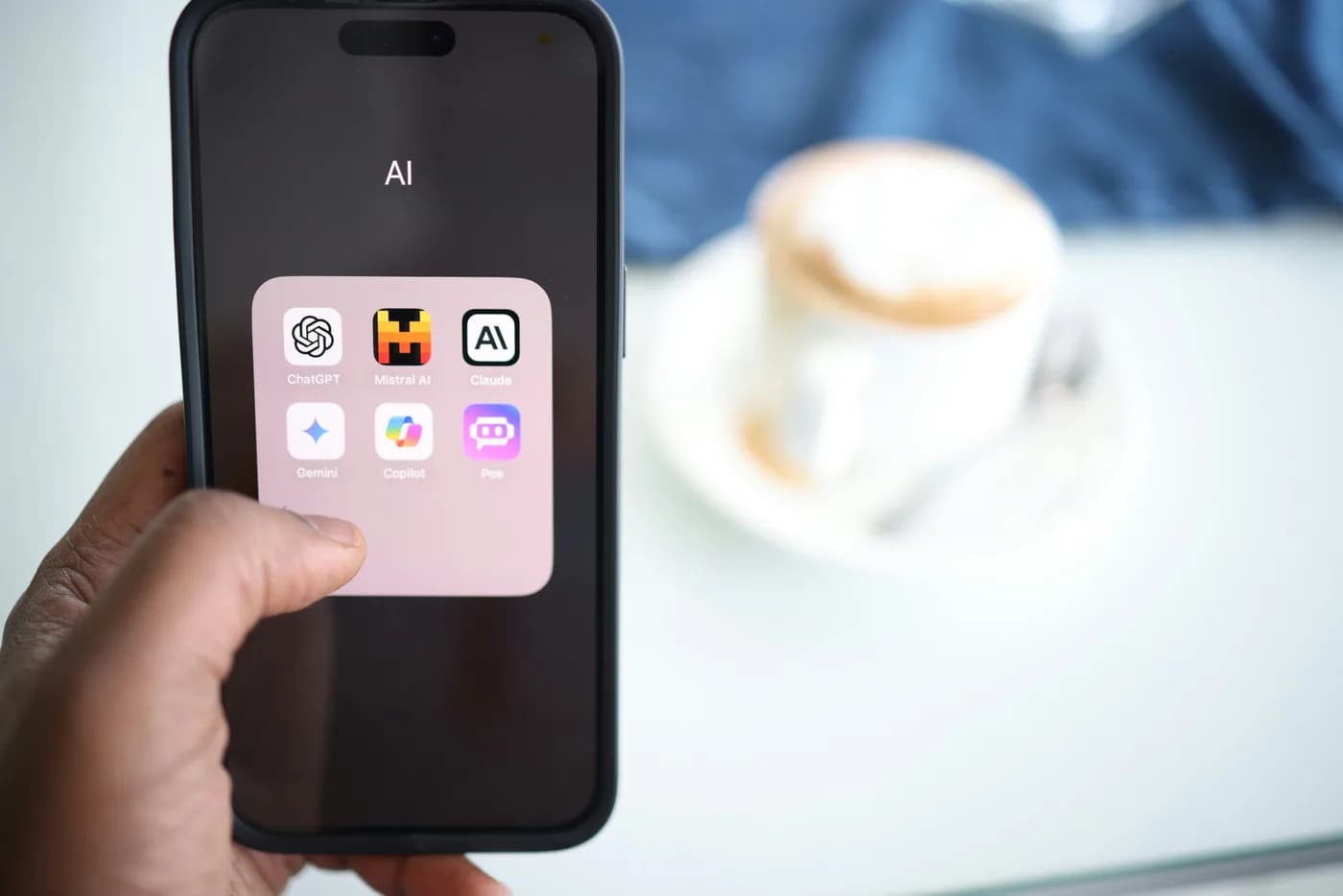 Mano sosteniendo un iPhone con aplicaciones de IA como ChatGPT, Claude y Gemini